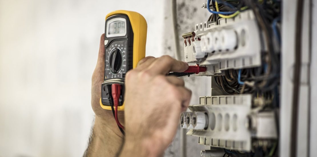 a male engineer testing an electrical fuse board with a multimeter