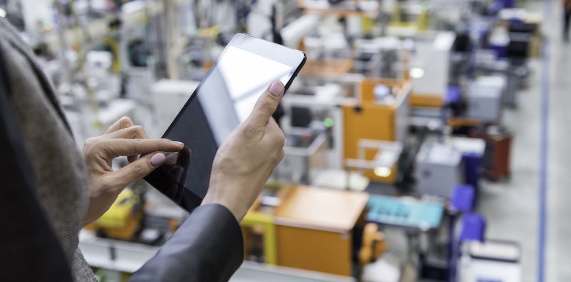 a woman using a tablet looking down on a factory floor